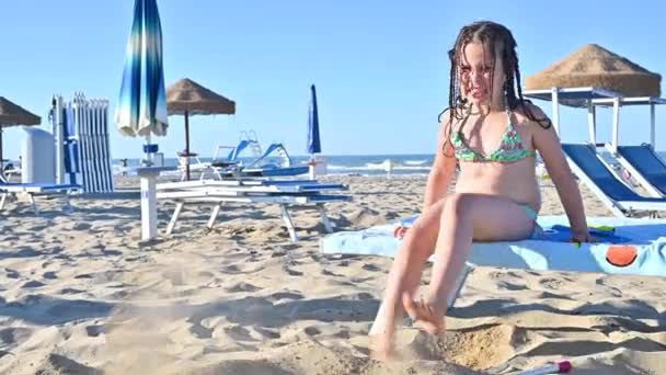 Kleines Mädchen im Badeanzug am Strand spielt, lächelt. Kind 7 Jahre alt am Strand von Italien. Das Konzept eines Sommer-, Familienurlaubs am Meer. Die Person zeigt positive Emotionen. — Stockvideo