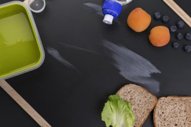 Okul yemeği siyah bir karatahtanın üzerinde. Öğrenciye ve beslenme çantasına yemek hazırlıyorum. Peynirli, meyveli ve suyla tost. Sağlıklı yiyecekler. İngilizce tebeşirle yazılmış. Hareketi Durdur. Üst görünüm