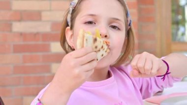 7 yaşındaki küçük kız pizza yiyor. Çocuk sokak yemekleriyle yemek yerken pozitif duygular ve zevk gösteriyor. İnce hamurlu geleneksel İtalyan pizzası..