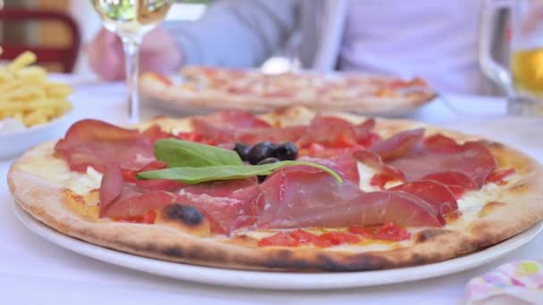 Dos grandes pizzas con jamón, albahaca, mozzarella en un restaurante italiano. Tradicional pizza italiana delgada norte y vino en la mesa. Almuerzo familiar. Algunos de los objetos están fuera de foco. — Vídeos de Stock