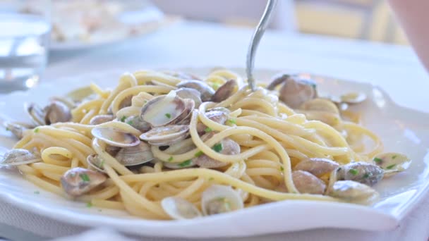 Makaron Vongole jest biały. Tradycyjne włoskie danie z małymi muszelkami i spaghetti. Człowiek nakręca jedzenie na widelcu w talerzu. Lunch we włoskiej restauracji z owocami morza. Miękkie skupienie — Wideo stockowe