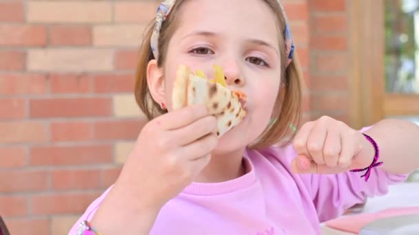 Klein meisje van 7 eet pizza. Het kind toont positieve emoties en plezier wanneer hij dineert met straatvoedsel. Traditionele Italiaanse pizza op dunne korst. — Stockvideo