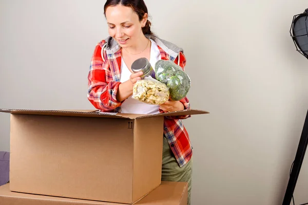 Het pakje uitpakken. De vrouw opent de doos en haalt graag de aankopen uit de online winkel. Levering en service concept. Online winkelen. De persoon is een Europeaan. Vrije ruimte voor tekst. — Stockfoto