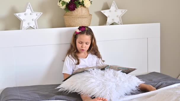 La estudiante está leyendo. Una niña leyendo un libro en el dormitorio de la cama. Educación y pasatiempos de los niños. Colores diurnos y claros. — Vídeos de Stock