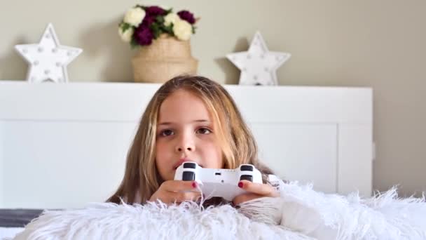 Mała dziewczynka gra na konsoli komputerowej na kanapie w jasnym pokoju. Równoczesne gry dla dzieci. Joystick dla kontroli w rękach. Emocje i zabawa dziecka. Odbiór. Wysokiej jakości materiał 4k — Wideo stockowe