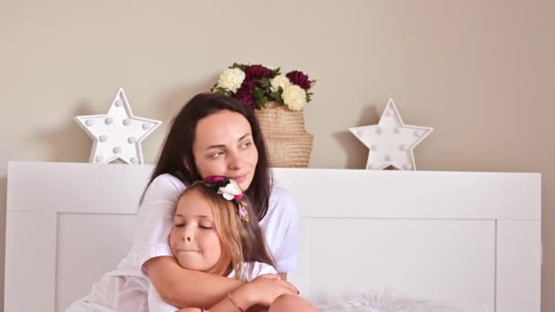 Anya és lánya ölelkeznek a hálószobában az ágyon. A gyengéd érzelmek megnyilvánulása, az anya és a gyermek kapcsolata. — Stock videók