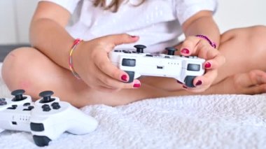 Bir çocuğun elinde bir bilgisayar oyunu için joystick, yakın plan. Küçük bir kız parlak bir odada bilgisayar konsolu oynuyor. Çocuklar ve ebeveynler için modern oyunlar. Uzayı kopyala Yüksek kalite 4k görüntü