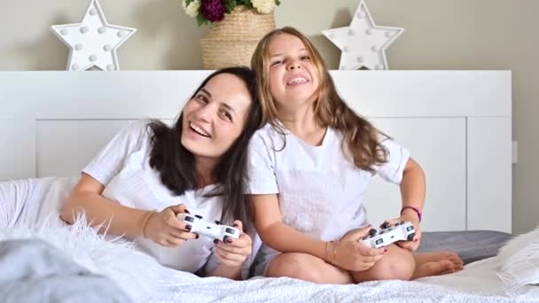 Mała dziewczynka i mama grają z mamą w grę komputerową. Jostycy w garści. Nowoczesne gry komputerowe dla dzieci i rodziców. Rozpowszechnianie radosnych emocji przez osoby. Wysokiej jakości materiał 4k — Wideo stockowe