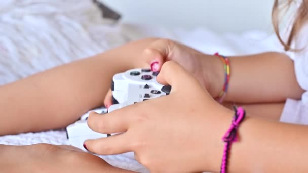 Joystick para un juego de ordenador en manos de un niño, de cerca. Una niña pequeña toca una consola de computadora en una habitación luminosa. Juegos modernos para niños y padres. — Vídeos de Stock