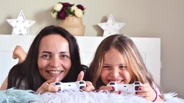 Το κοριτσάκι και η μαμά παίζουν ηλεκτρονικό παιχνίδι με τη μαμά. Οι Τζόστικς είναι στο χέρι. Σύγχρονα ηλεκτρονικά παιχνίδια για παιδιά και γονείς. Διάδοση χαρούμενων συναισθημάτων από άτομα. Υψηλής ποιότητας 4k πλάνα — Αρχείο Βίντεο