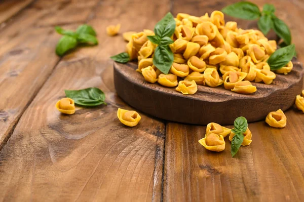 Tortellini mignon ahşap bir tahtada fesleğen ve parmesanlı. Bologna ve Emilia Romagna mutfağının spesiyaliteleri: Cappelletti, et ve sebzeli taze yumurtalı makarna..
