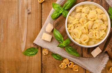 Tortellini mignon ahşap bir tahtada fesleğen ve parmesanlı. Bologna ve Emilia Romagna mutfağının spesiyaliteleri: Cappelletti, et ve sebzeli taze yumurtalı makarna..