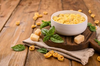 Tortellini mignon ahşap bir tahtada fesleğen ve parmesanlı. Bologna ve Emilia Romagna mutfağının spesiyaliteleri: Cappelletti, et ve sebzeli taze yumurtalı makarna..