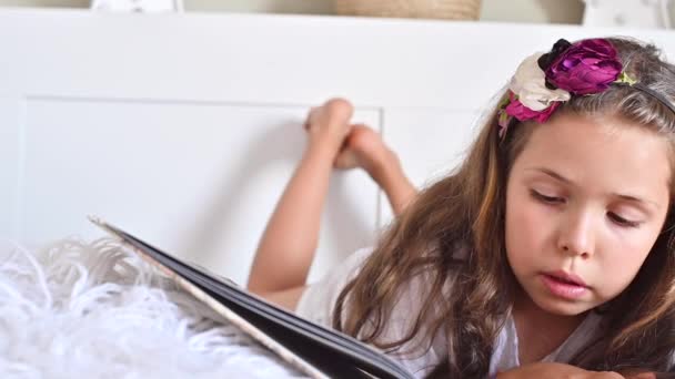 La estudiante está leyendo. Una niña leyendo un libro en el dormitorio de la cama. Educación y pasatiempos de los niños. Colores diurnos y claros. — Vídeos de Stock