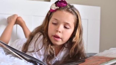 Liseli kız okuyor. Yatak odasında yatakta kitap okuyan küçük bir kız. Çocukların eğitimi ve hobileri. Gündüz ve açık renk.