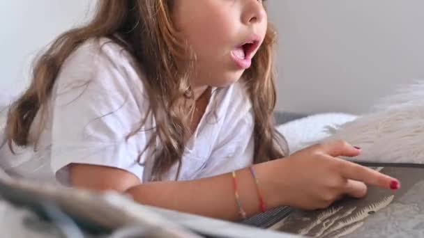 Die Schülerin liest. Kleines Mädchen beim Lesen eines Buches im Schlafzimmer auf dem Bett. Bildung und Hobbys der Kinder. Tageszeit und helle Farben. — Stockvideo