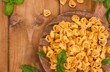 Tortellini mignon ahşap bir tahtada fesleğen ve parmesanlı. Bologna ve Emilia Romagna mutfağının spesiyaliteleri: Cappelletti, et ve sebzeli taze yumurtalı makarna..