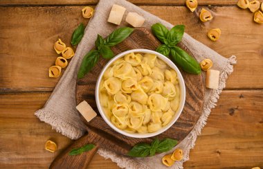 Tortellini mignon ahşap bir tahtada fesleğen ve parmesanlı. Bologna ve Emilia Romagna mutfağının spesiyaliteleri: Cappelletti, et ve sebzeli taze yumurtalı makarna..