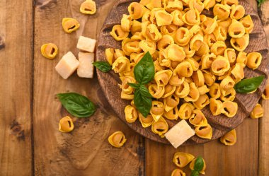Tortellini mignon ahşap bir tahtada fesleğen ve parmesanlı. Bologna ve Emilia Romagna mutfağının spesiyaliteleri: Cappelletti, et ve sebzeli taze yumurtalı makarna..