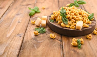 Tortellini mignon ahşap bir tahtada fesleğen ve parmesanlı. Bologna ve Emilia Romagna mutfağının spesiyaliteleri: Cappelletti, et ve sebzeli taze yumurtalı makarna..