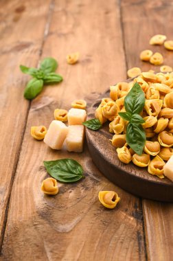 Tortellini mignon ahşap bir tahtada fesleğen ve parmesanlı. Bologna ve Emilia Romagna mutfağının spesiyaliteleri: Cappelletti, et ve sebzeli taze yumurtalı makarna..