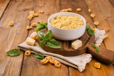 Tortellini mignon ahşap bir tahtada fesleğen ve parmesanlı. Bologna ve Emilia Romagna mutfağının spesiyaliteleri: Cappelletti, et ve sebzeli taze yumurtalı makarna..