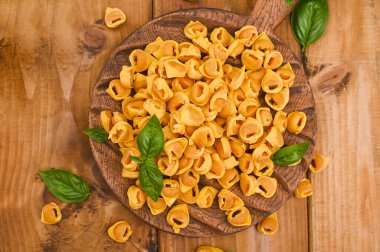 Tortellini mignon ahşap bir tahtada fesleğen ve parmesanlı. Bologna ve Emilia Romagna mutfağının spesiyaliteleri: Cappelletti, et ve sebzeli taze yumurtalı makarna..