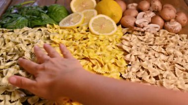Çeşitli kuru İtalyan makarnaları. Ispanak, mantar ve limon aromalı. El makarna alır..