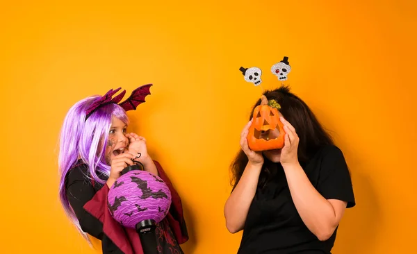 Veselý holčička v karnevalu kostým pro Halloween a maminka na žlutém pozadí ve studiu. — Stock fotografie