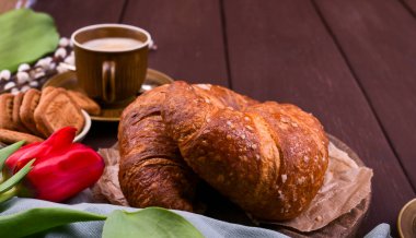 Paskalya kahvaltısında aromatik taze espresso, kruvasan, renkli yumurta, kırmızı lale ve söğüt. Kurabiyeli kahve, ahşap masadaki çiçekler. Yukarıdan bak. Boşluğu kopyala.