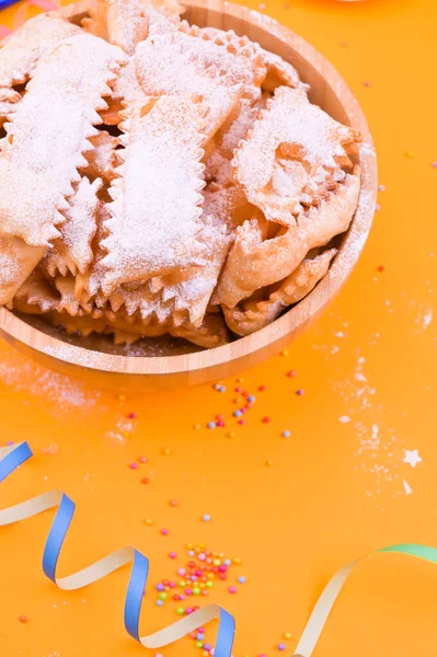 Traditional Italian carnival fritters dusted with icing sugar - frappe or chiacchiere . Sweets and festive decor on a yellow background. Free space for text. — Stock Photo, Image