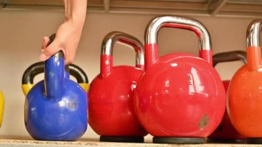 Spor salonunun rafında farklı renkte dambıllar ve ağırlıklar var. Kadın bir spor malzemesi alıyor. Yerleşim odağı
