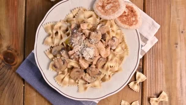 Bord met pasta met champignons bovenaanzicht. Vlinderpasta met champignons en parmezaanse kaassaus. Typische Italiaanse keuken uit het zuiden van Italië. — Stockvideo
