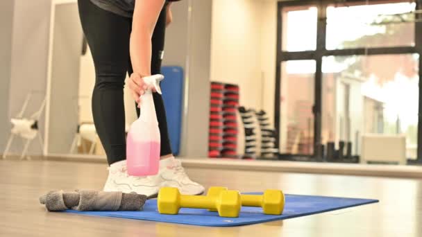 Sportlerin desinfiziert Sportmatte nach dem Training mit einem Antiseptikum. Maßnahmen, die während der COVID 19 in der Sporthalle zu ergreifen sind. — Stockvideo