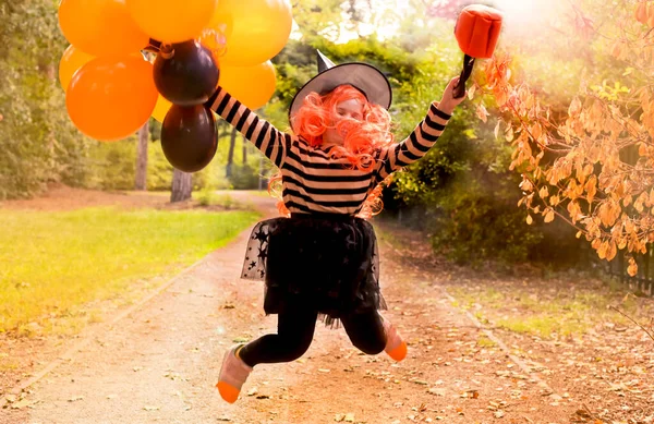 Happy holiday Halloween. Little cheerful girl in a witch costume and colored balloons. Sun glare in the frame. Soft focus. — Stock Photo, Image