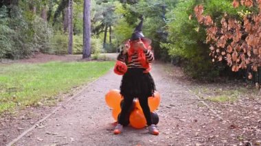 Cadı kostümlü küçük neşeli kız atlıyor ve parkta balonlarla eğleniyor. Mutlu bayramlar. Çerçevede güneş parlıyor. Ana konuya odaklanın..