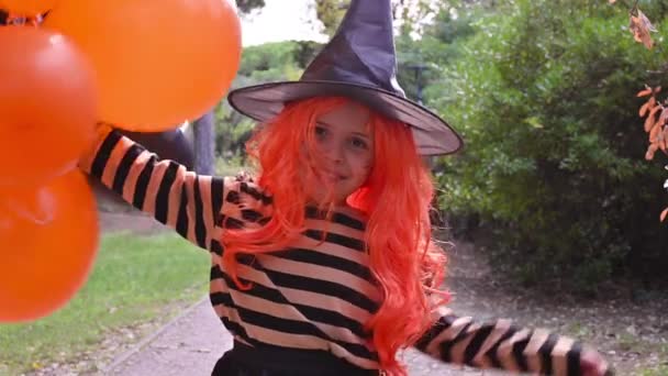 Petite fille habillée en sorcière avec une barre chocolatée dans un parc d'automne. Joyeuses vacances d'Halloween. La mise au point est douce déplacé sur l'objet principal. — Video