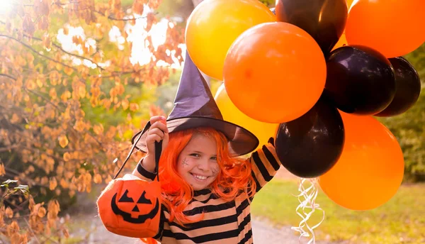 Dítě v karnevalovém kostýmu na Halloween s velkými barevnými balónky. Holčička v podzimním parku. Fokus je posunut na hlavní objekt. — Stock fotografie