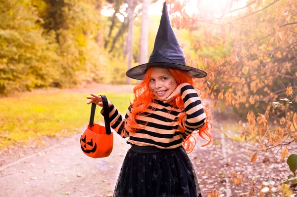 Holčička převlečená za čarodějku s tyčinkou v podzimním parku. Šťastný Halloween. Fokus je posunut na hlavní objekt. — Stock fotografie
