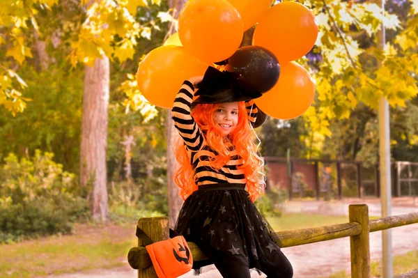 Een kind in een carnaval kostuum op Halloween met grote gekleurde ballonnen. Klein meisje in het herfstpark. De focus is zacht verschoven naar het hoofddoel. — Stockfoto