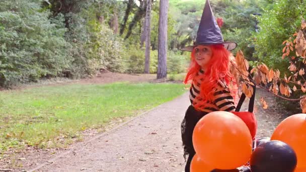 Een kind in een carnaval kostuum op Halloween met grote gekleurde ballonnen. Klein meisje in het herfstpark. De focus is zacht verschoven naar het hoofddoel. — Stockvideo