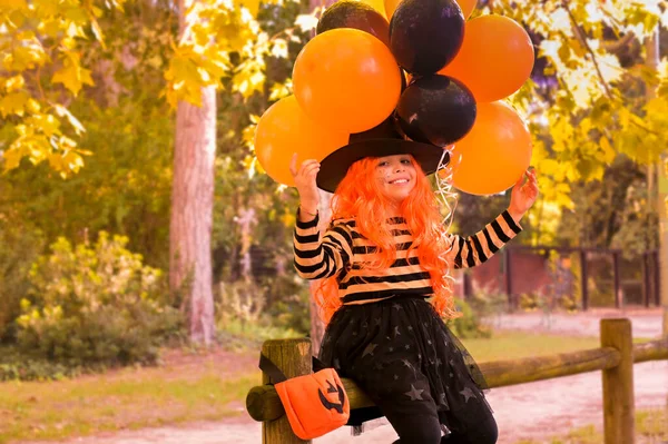 Ένα παιδί σε ένα καρναβάλι κοστούμι στις Απόκριες με μεγάλα χρωματιστά μπαλόνια. Κοριτσάκι στο φθινοπωρινό πάρκο. Η εστίαση είναι μαλακή μετατοπίζεται στο κύριο αντικείμενο. — Φωτογραφία Αρχείου
