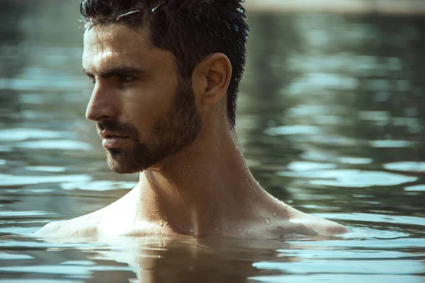 Strong face male model on the nature background with sand and water on the beach on the sunset