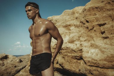 Güçlü yüz kaslı erkek model kum kayalar ve gün batımı sahilde su Doğa arka plan üzerinde