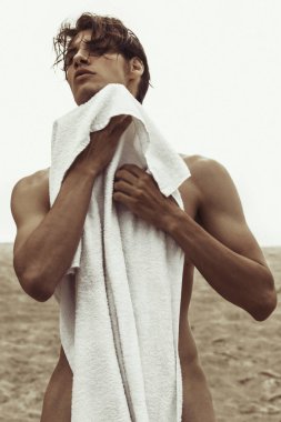 Seksi güzel çizgili erkek model kum ile doğa arka plan üzerinde beyaz havlu ve gökyüzü günbatımı üzerinde sahilde