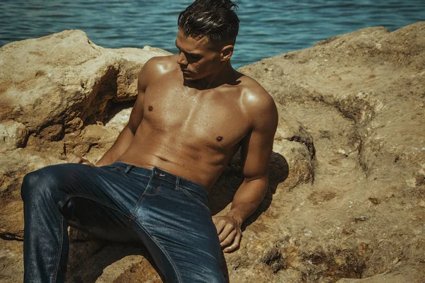 Strong face muscled male model on the nature background with sand rocks  and water on the beach on the sunset