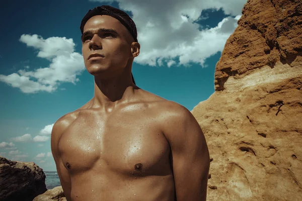 Strong face muscled male model on the nature background with sand rocks  and water on the beach on the sunset