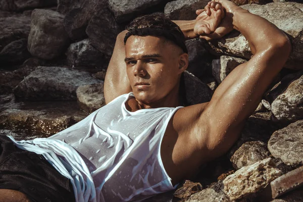 Strong face muscled male model on the nature background with sand rocks  and water on the beach on the sunset