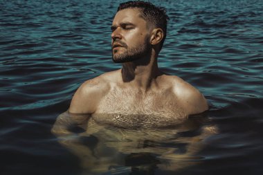Seksi güçlü sakallı erkek yakışıklı yaz vibes ile su arka plan üzerinde kırmızı yüzmek şortlu