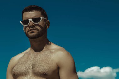 Kum ve mavi gökyüzü bulutlu üzerinde beyaz sunglesses kot ve beyaz tişört giyen güçlü ticari yüz erkek modeli 